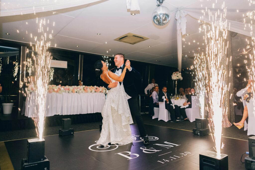Bride and groom share a romantic dance surrounded by sparkling fireworks indoors.